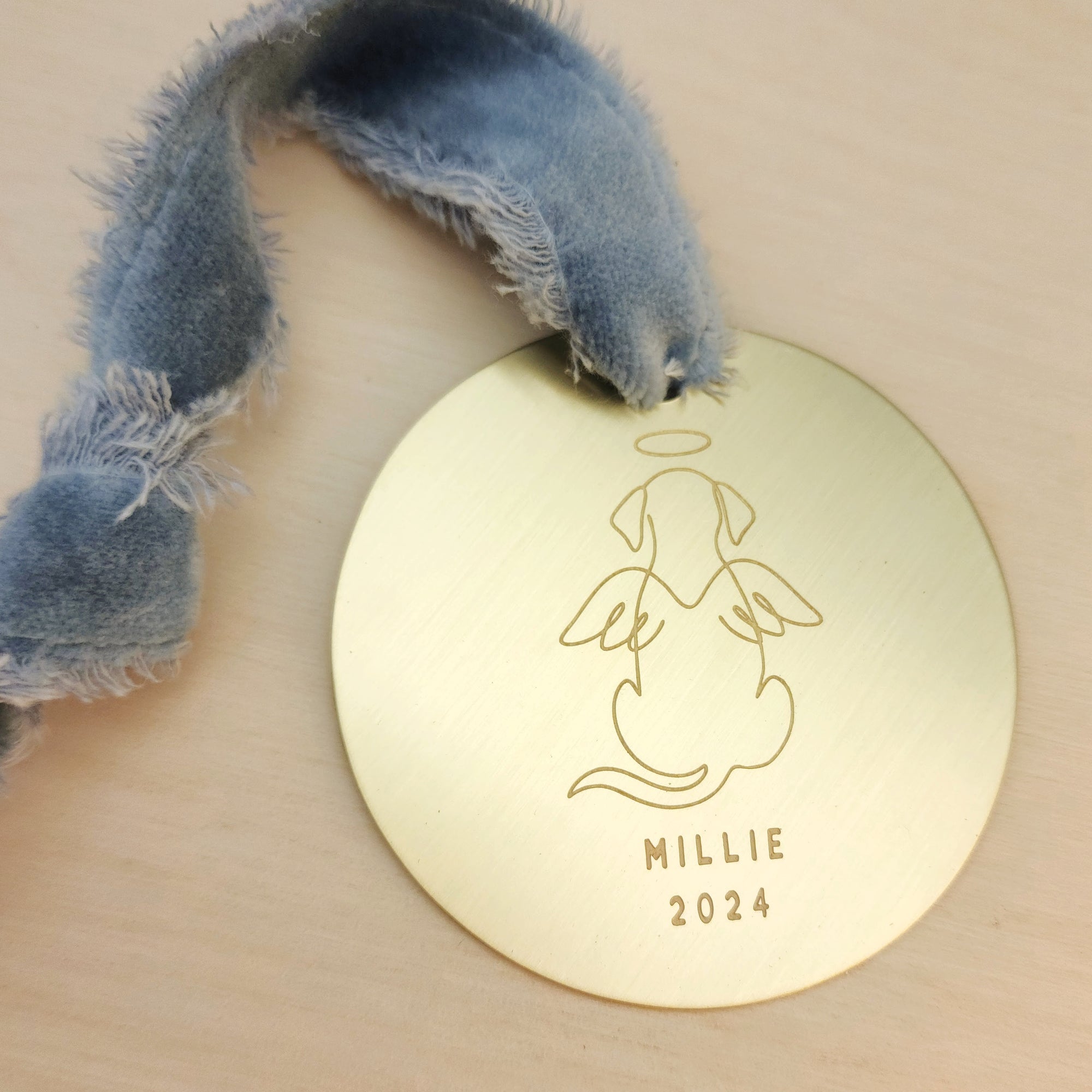Gold tag with dog illustration and 'MILLIE 2024' text, attached to a ribbon.
