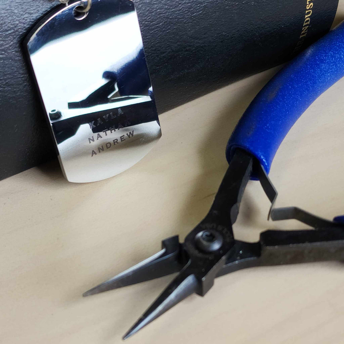 Pair of pliers with blue handle on a beige surface, next to a metal tag.