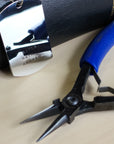 Pair of pliers with blue handle on a beige surface, next to a metal tag.