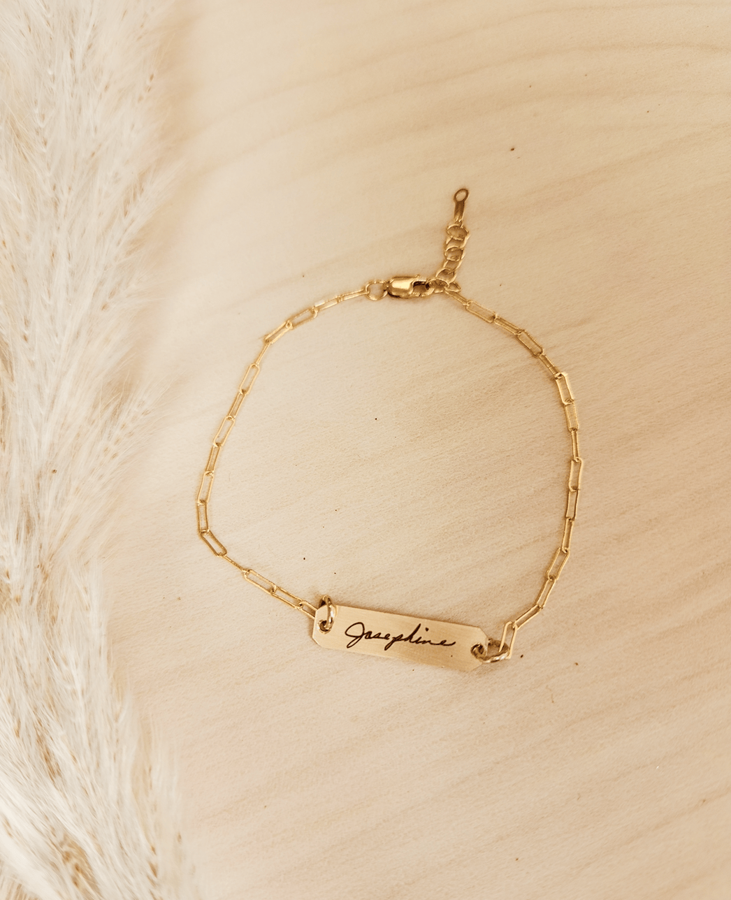 A gold-filled bracelet with a personalized signature tag on a person's wrist, showing the name 'Josephine'.