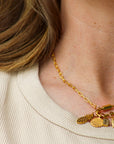 Gold necklace with charms worn by a person against a neutral background