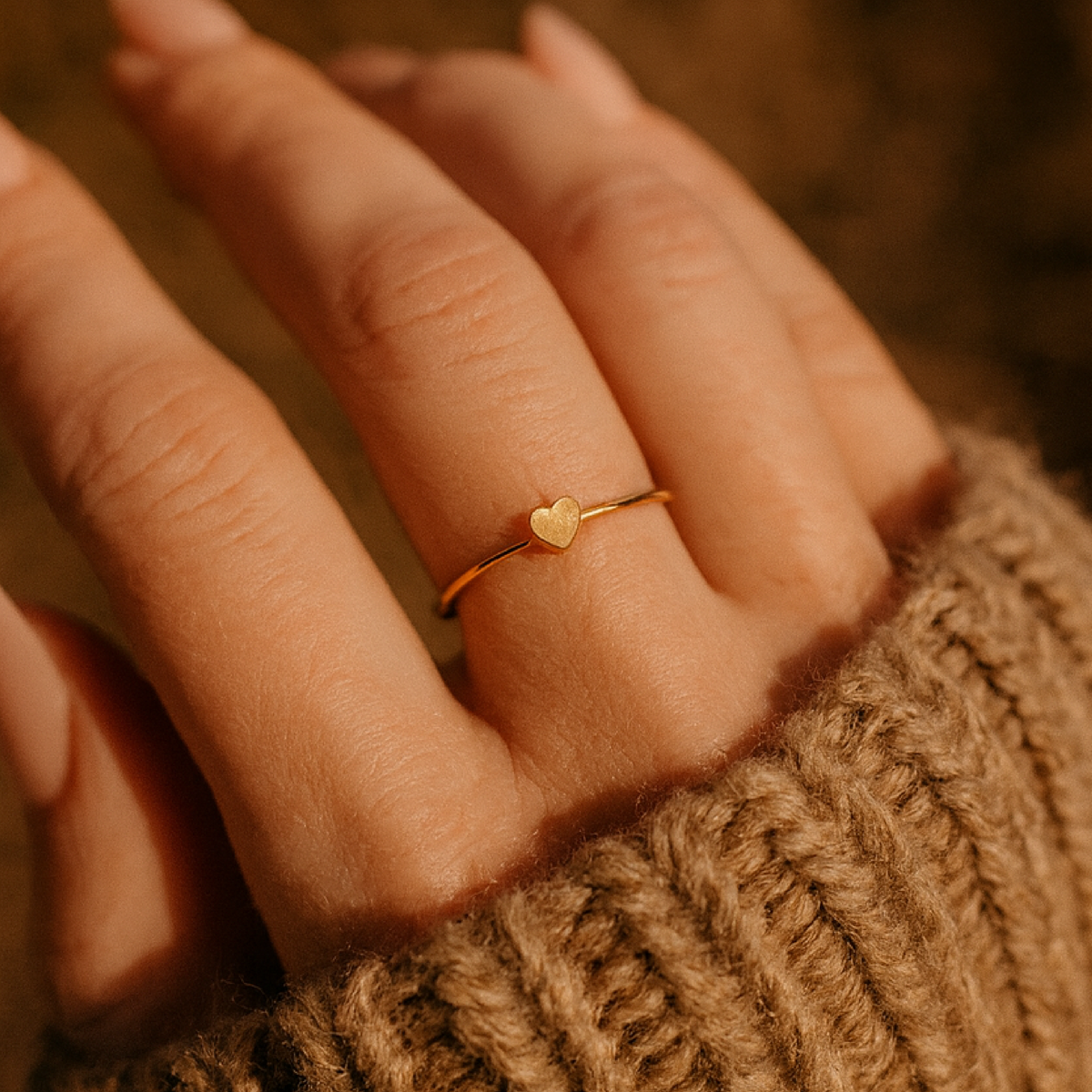 Close-up of a hand wearing a gold heart-shaped ring on a textured brown background