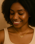Woman wearing a gold necklace with a heart-shaped pendant against a neutral background