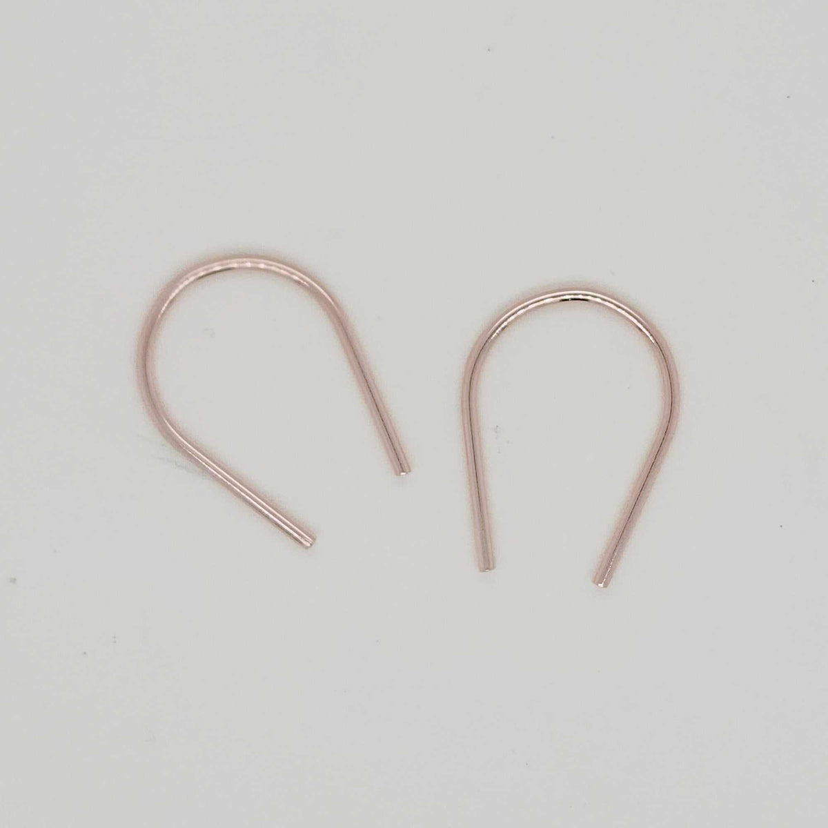 Dainty gold U-shaped earrings flat lay on cream surface