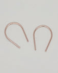 Dainty gold U-shaped earrings flat lay on cream surface