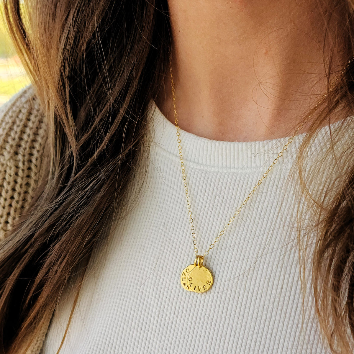 Gold necklace with a round pendant worn by a person against a neutral background