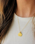 Gold necklace with a round pendant worn by a person against a neutral background