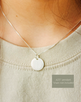 Close-up of a silver pendant necklace on a person wearing a light green top.