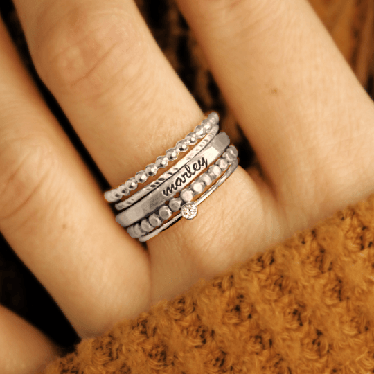 five silver rings, one ring is personalized with a name, shown on a woman's hand