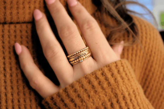 a woman in a brown shirt is holding up her hand, showing her gold ring set