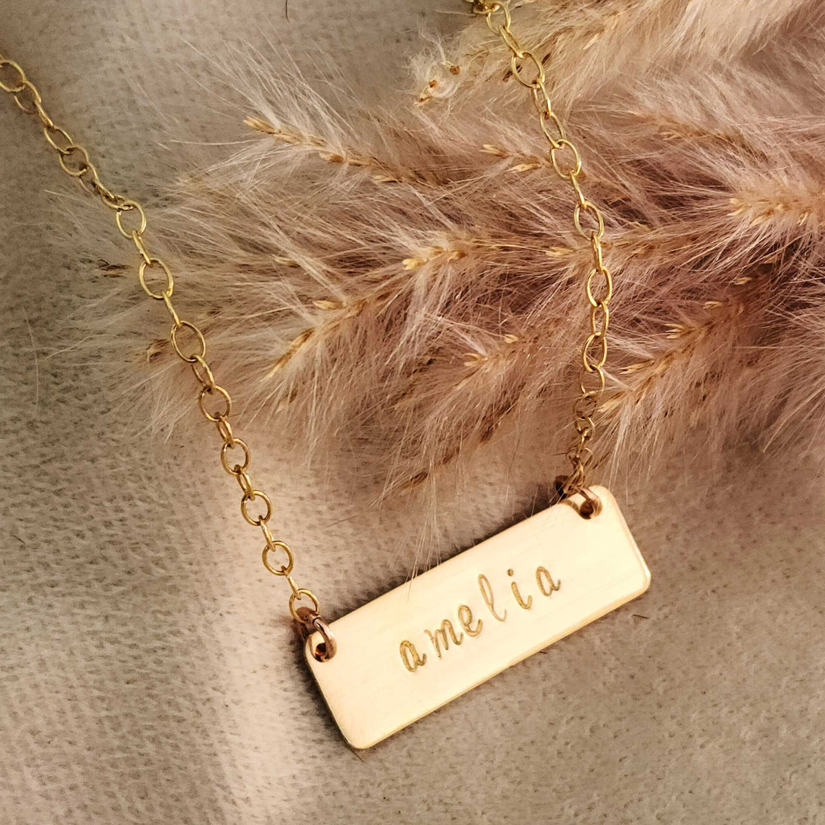 Short gold bar necklace with custom stamped name and brushed finish on an adjustable chain