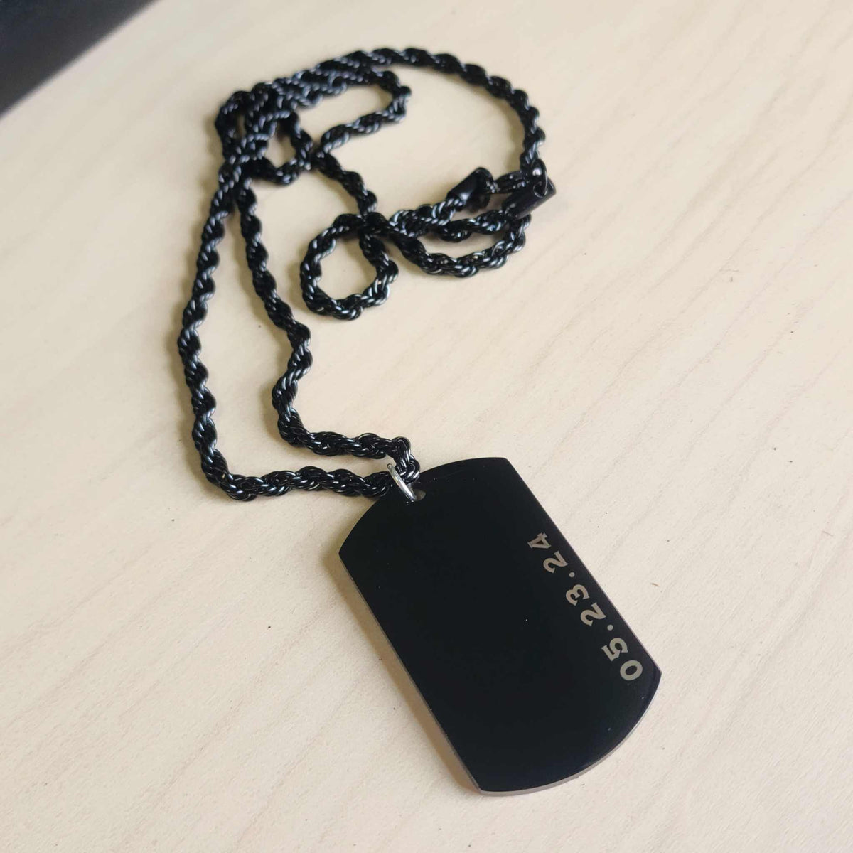 Black dog tag pendant on a chain against a beige background