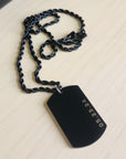 Black dog tag pendant on a chain against a beige background
