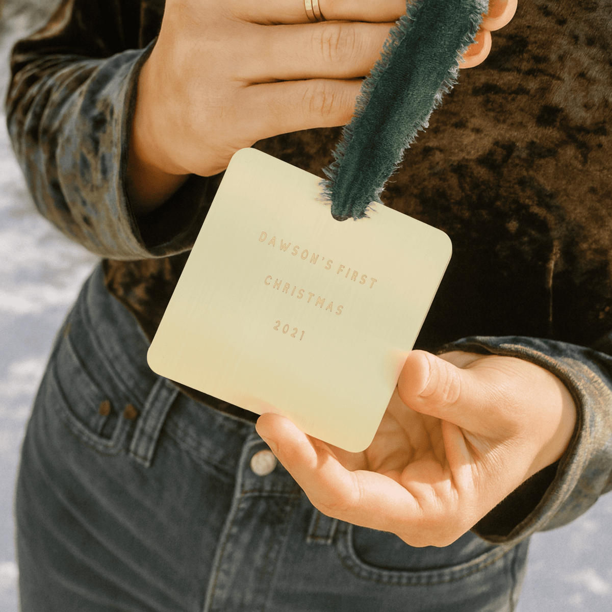 Hand holding a small square card with 'Dawson's First Christmas 2021' text, with a green felt ornament.