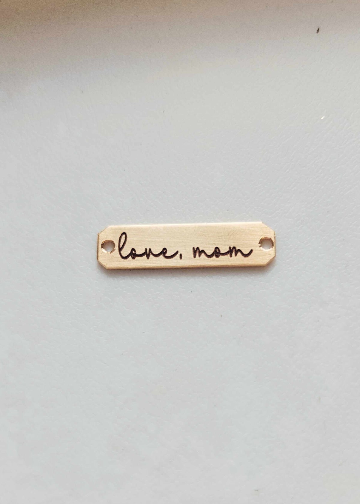 A double-sided wooden handwriting connector bar with the inscription 'Love Mom' engraved on it, placed on a white surface.