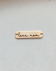 A double-sided wooden handwriting connector bar with the inscription 'Love Mom' engraved on it, placed on a white surface.