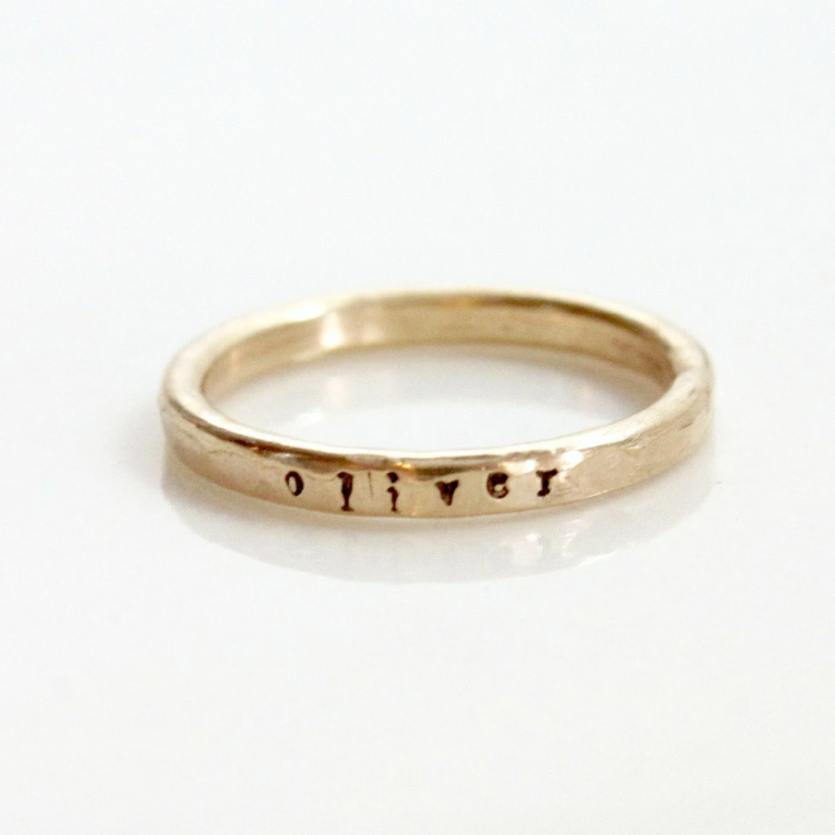 Close-up of a delicate tiny font stacking name ring in 14k rose gold filled, 2mm tall and expertly handcrafted