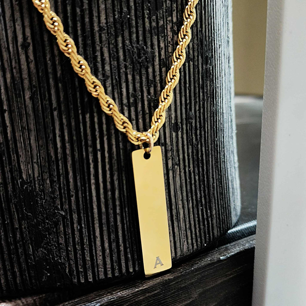 Gold necklace with a rectangular pendant on a wooden surface