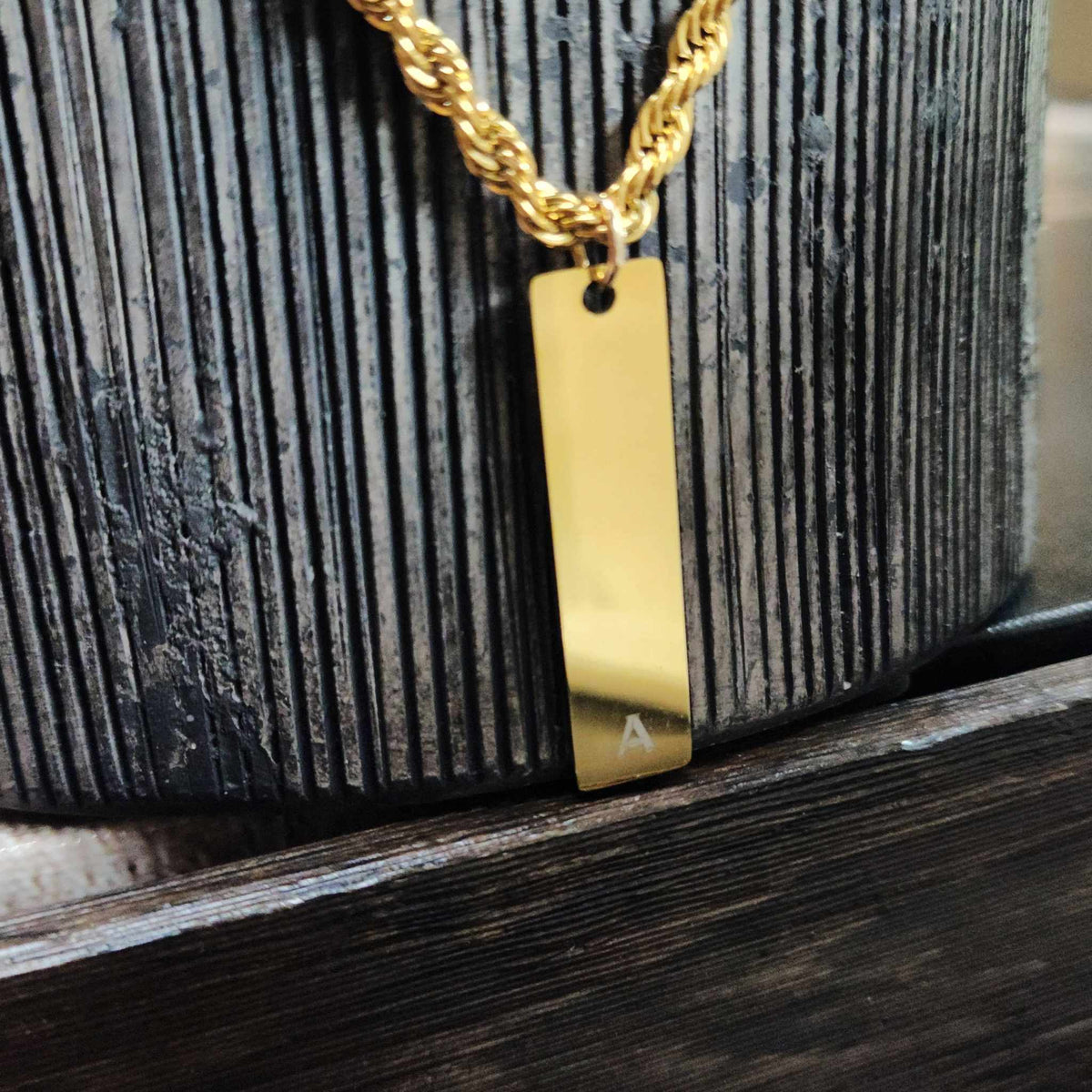 Gold necklace with a rectangular pendant on a textured surface