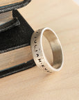 Silver ring with engraved text on a textured surface with books in the background