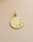 Gold pendant with engraved text on a beige background