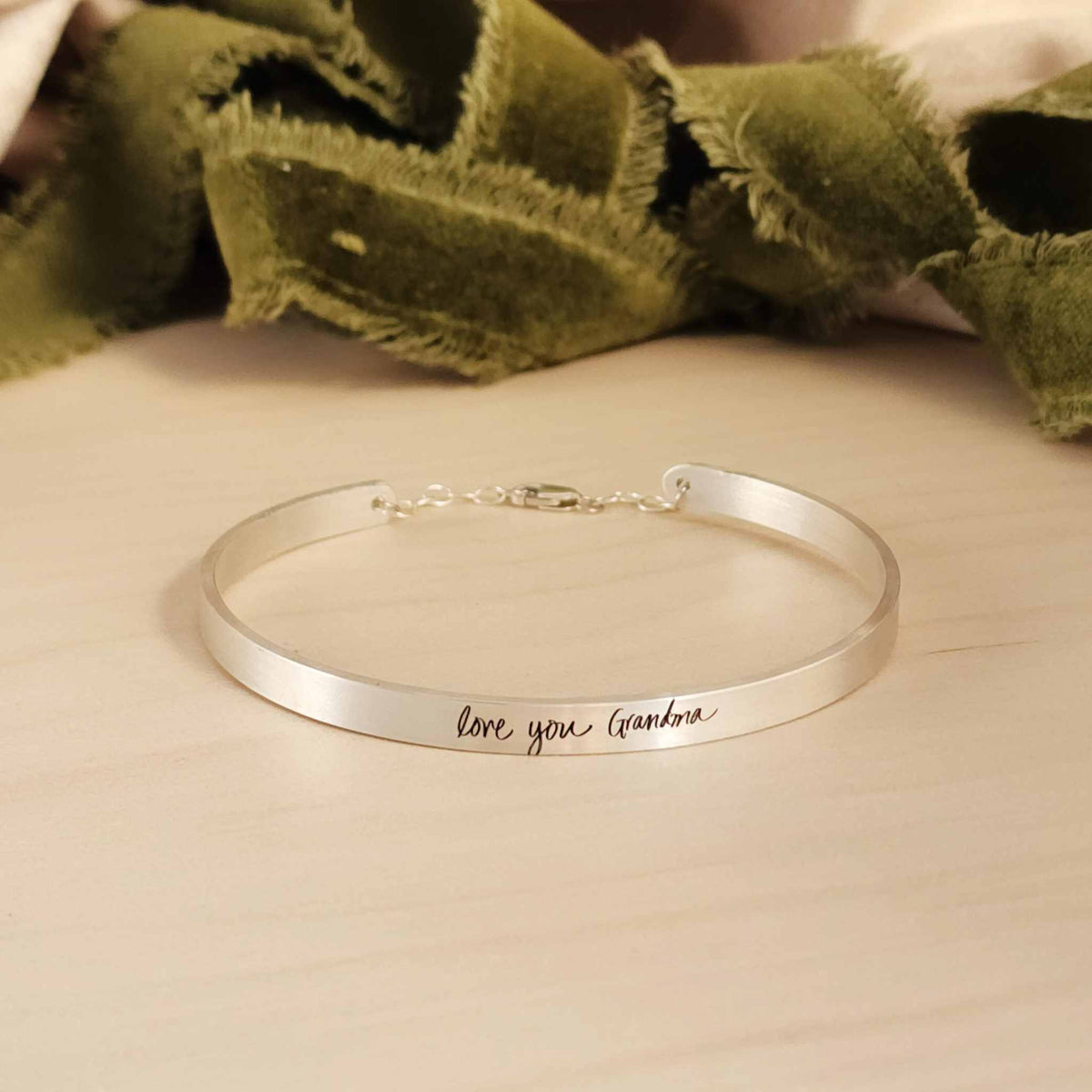 silver cuff bracelet on wood with green ribbon in background