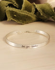silver cuff bracelet on wood with green ribbon in background