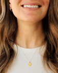 Close-up of a woman wearing a gold necklace with a pendant, smiling.