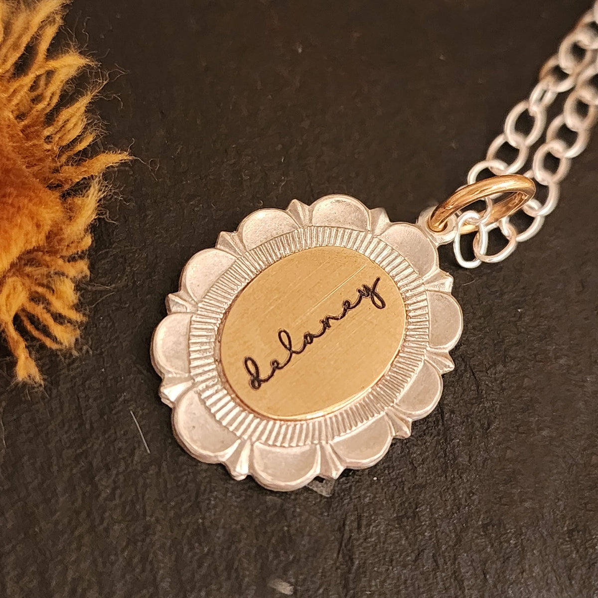 Gold and silver necklace with a floral pendant on a dark surface