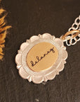 Gold and silver necklace with a floral pendant on a dark surface
