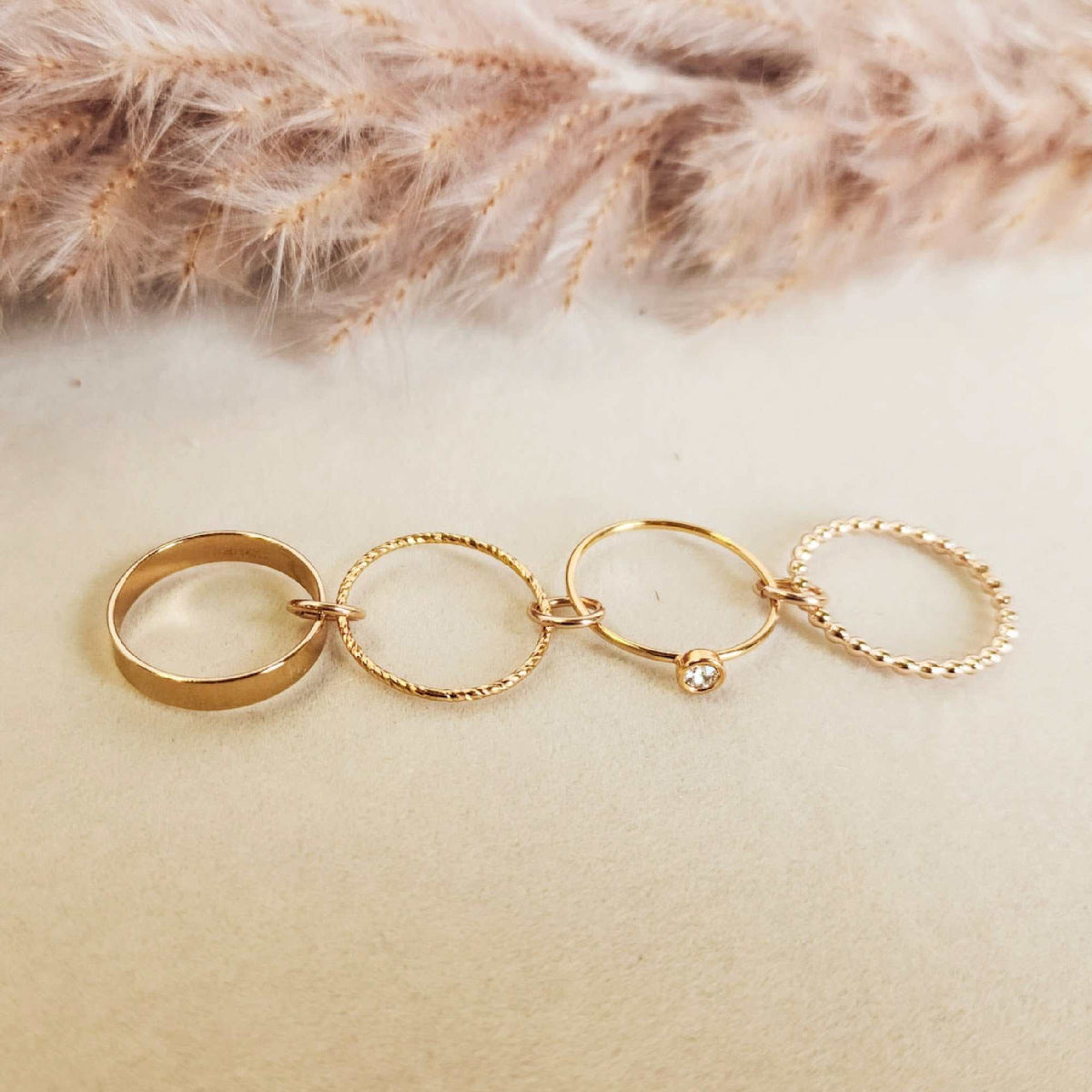 Set of gold rings on a soft beige surface with pampas grass in the background