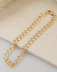 A gold double cable chain bracelet resting on a beige surface.