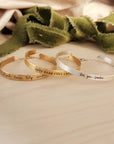 gold and silver handwriting cuff bracelet on wood table