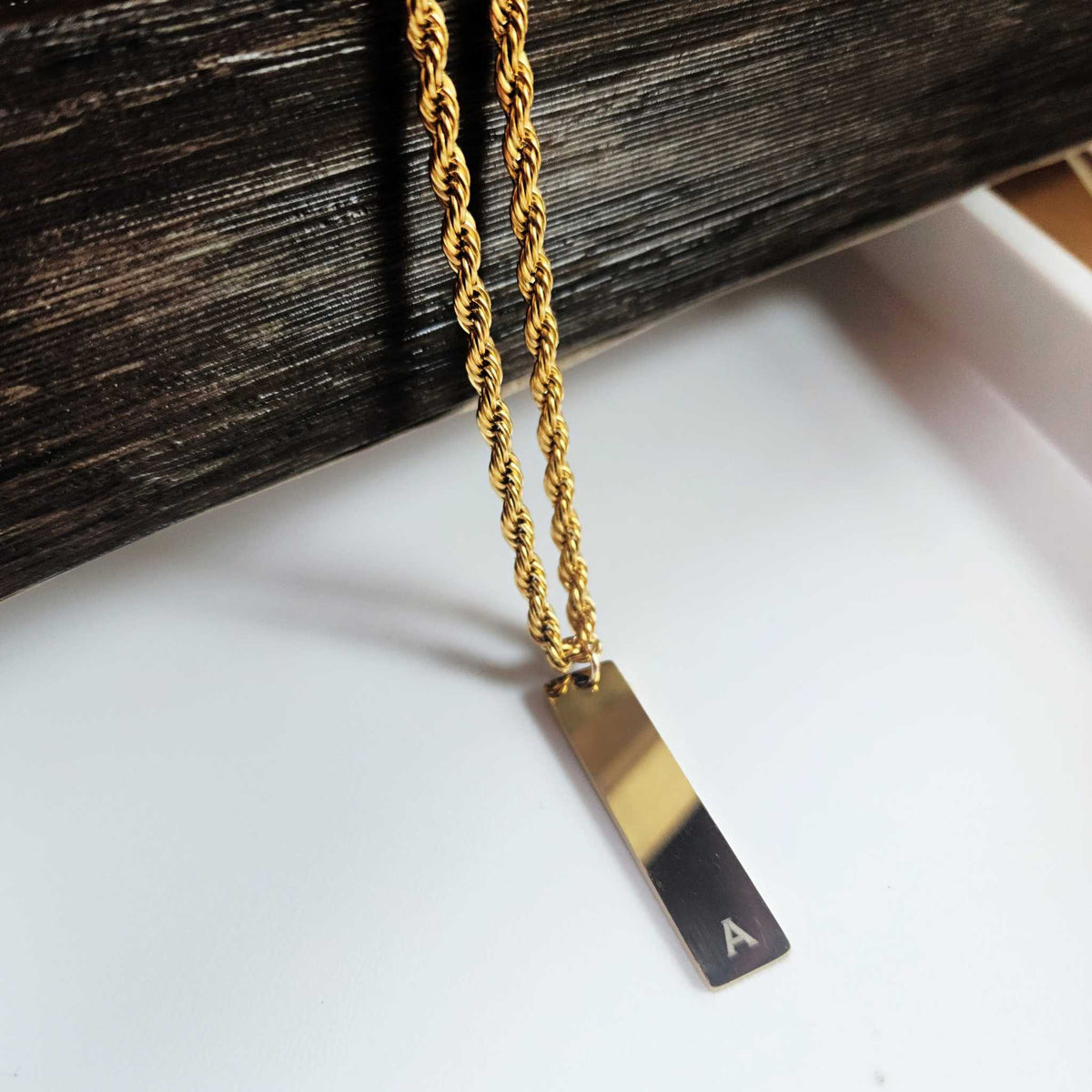 Gold necklace with a rectangular pendant on a white surface