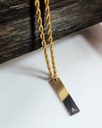 Gold necklace with a rectangular pendant on a white surface