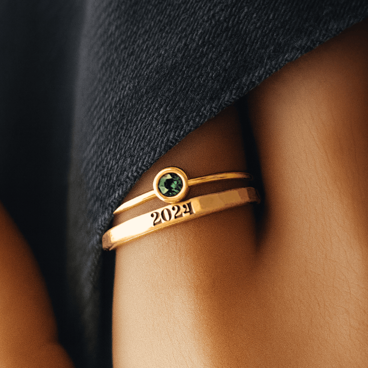 Gold ring with a green gemstone and '2024' on a person's finger against a dark fabric background