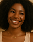 Woman with a warm smile wearing a beige tank top and gold necklace against a neutral background