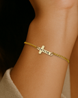 Gold bracelet with a cross charm on a wrist against a neutral background
