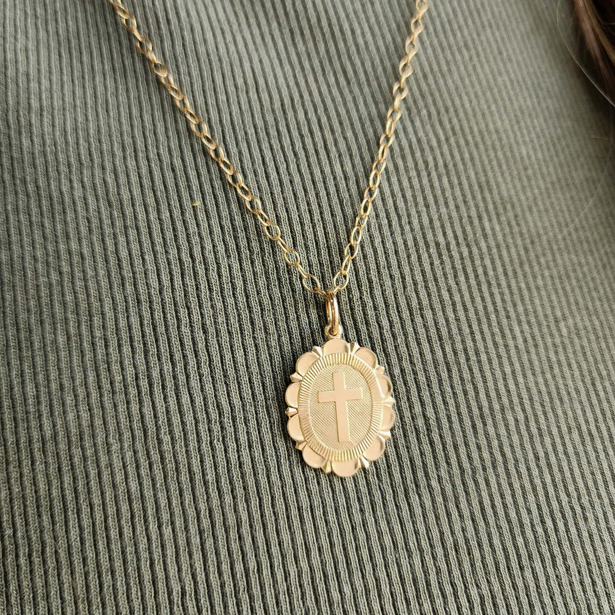 Gold necklace with a cross pendant on a textured green surface