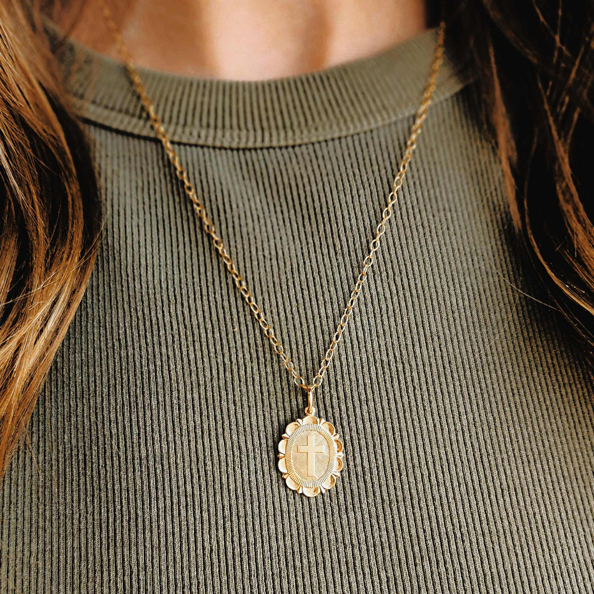 Personalized cross pendant necklace with polished cross and scalloped edge on textured oval backdrop, custom engraved on back, hanging from 18" cable chain