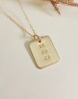 Gold date-stamped pendant necklace on gold chain displayed on a white background with gold leaf accent.