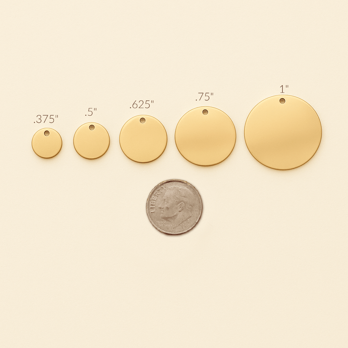 Gold circular pendants of different sizes with a coin for scale on a beige background