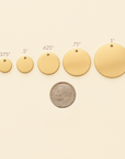 Gold circular pendants of different sizes with a coin for scale on a beige background