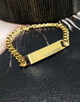 Gold chain bracelet with engraved tag on a textured black surface