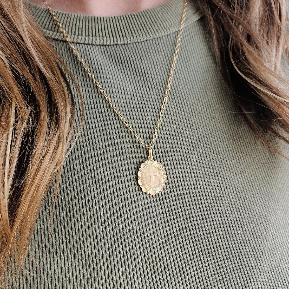 Gold necklace with a pendant on a person wearing a green ribbed sweater