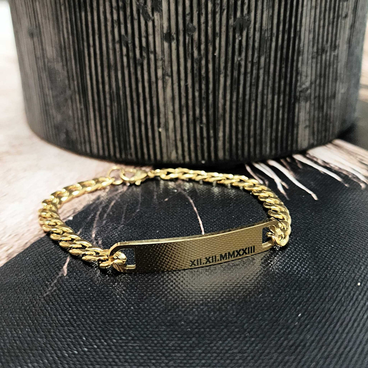 Gold chain bracelet with engraved text on a black textured surface