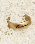 Gold ring with 'Liam' engraving on a white pebble background