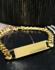 Gold chain bracelet with a engraved tag on a black textured surface