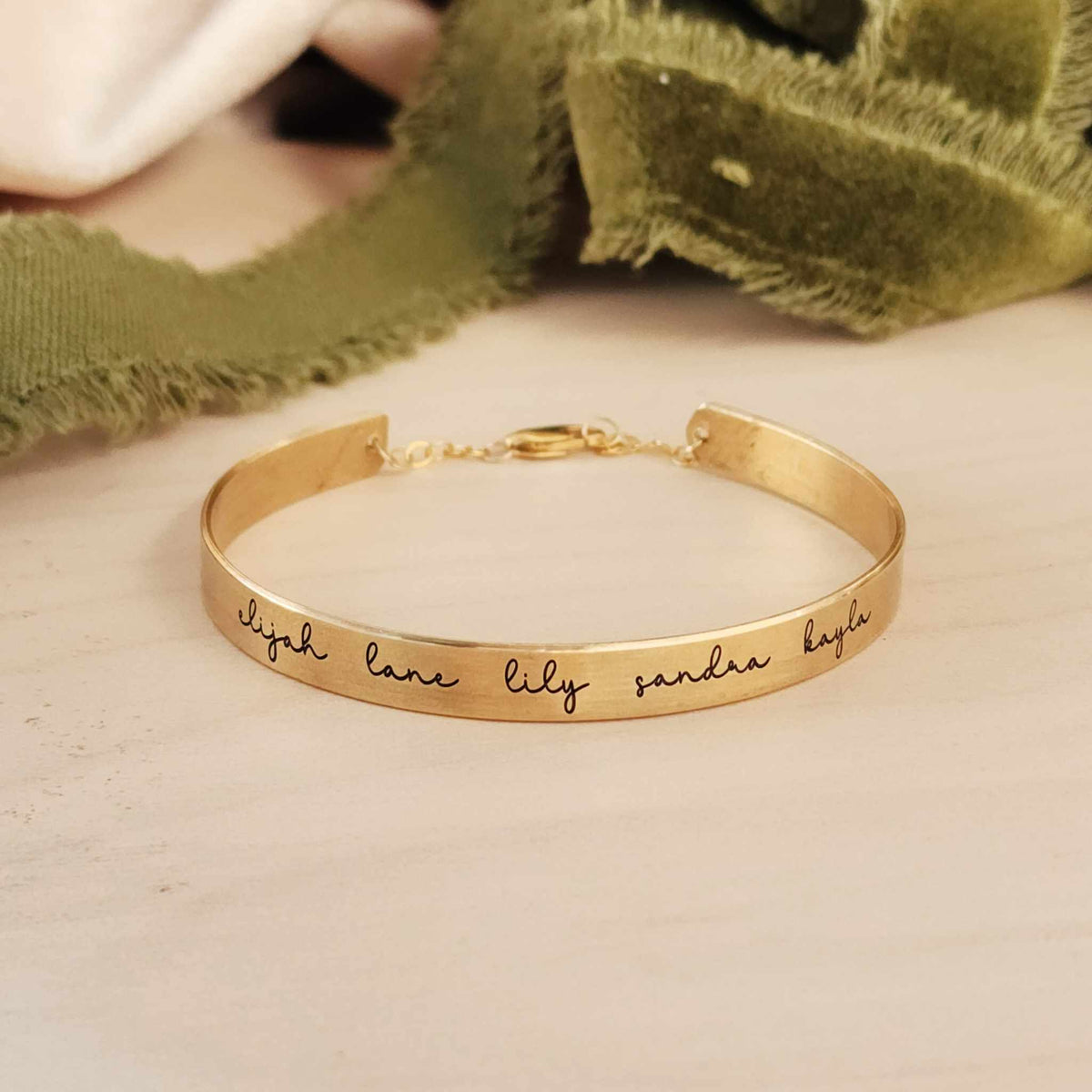 A gold-colored cuff bracelet with custom names engraved on it