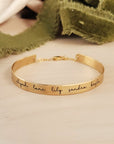 A gold-colored cuff bracelet with custom names engraved on it